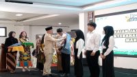 Pemasangan almamater secara simbolis ke perwakilan mahasiswa baru ISBI Kaltim oleh Kepala Disdikbud Kukar Heriansyah. (M. As'ari/Lingkar Kaltim)